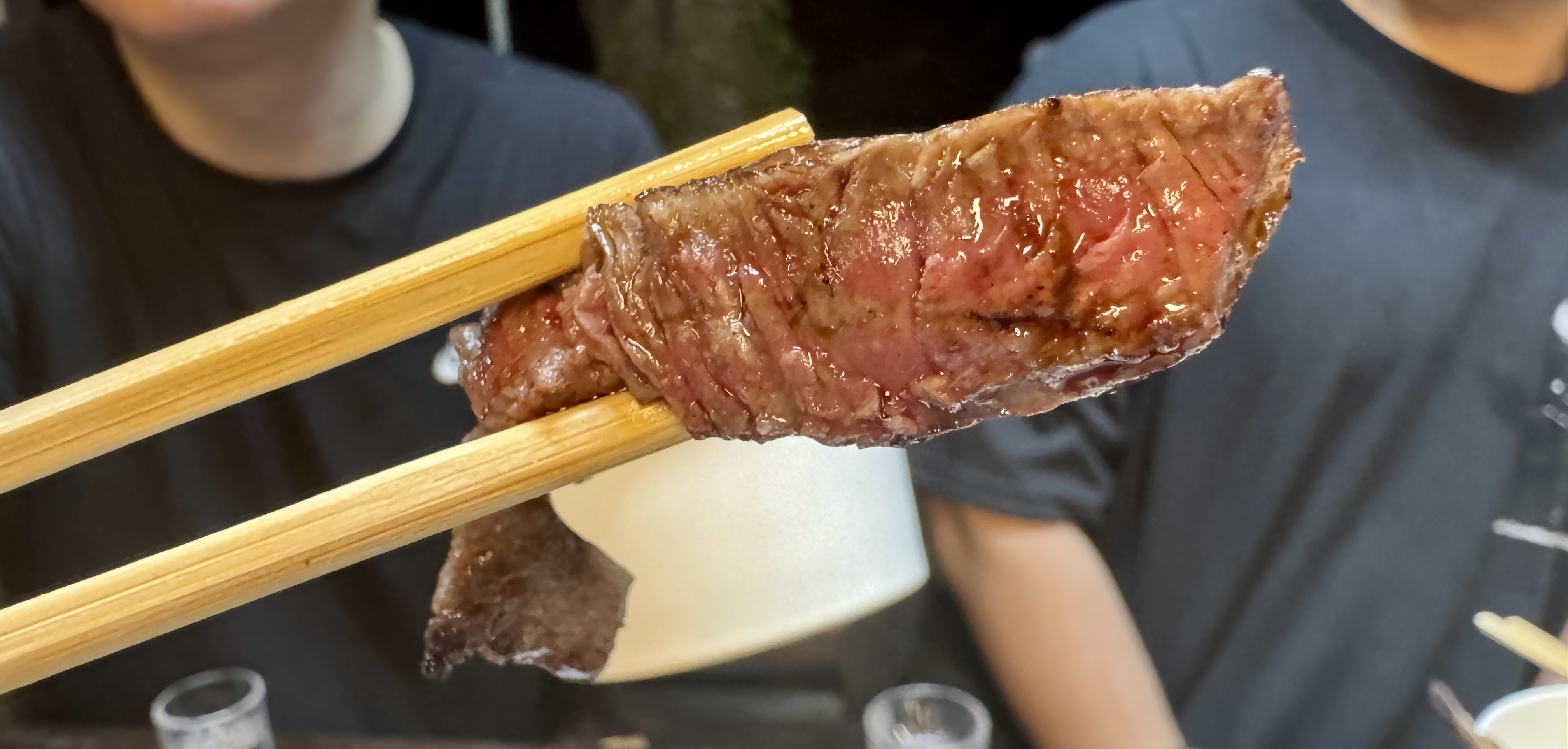 젓가락 사이에 집힌 한우 한 점. 겉은 바삭, 속은 촉촉하게 익은 단면이 선명하게 보인다.