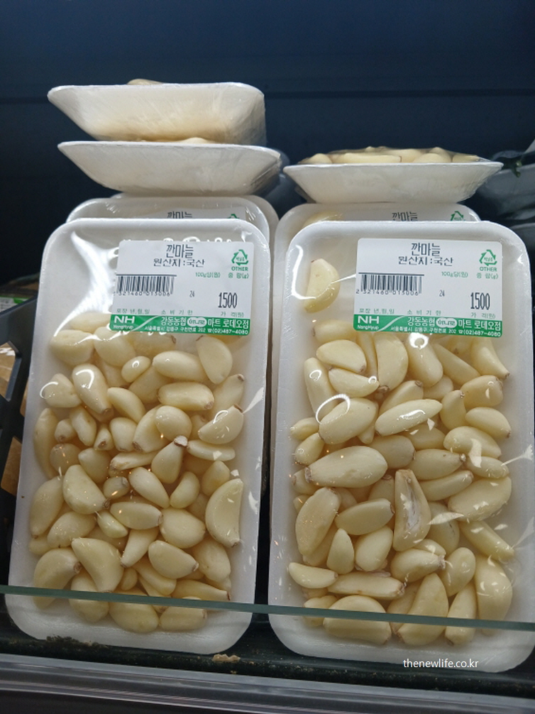 소포장 트레이에 담긴 깐마늘 제품이 냉장 진열대에 놓여 있는 사진으로, 생마늘을 소량으로 간편하게 구매하는 형태를 보여줍니다