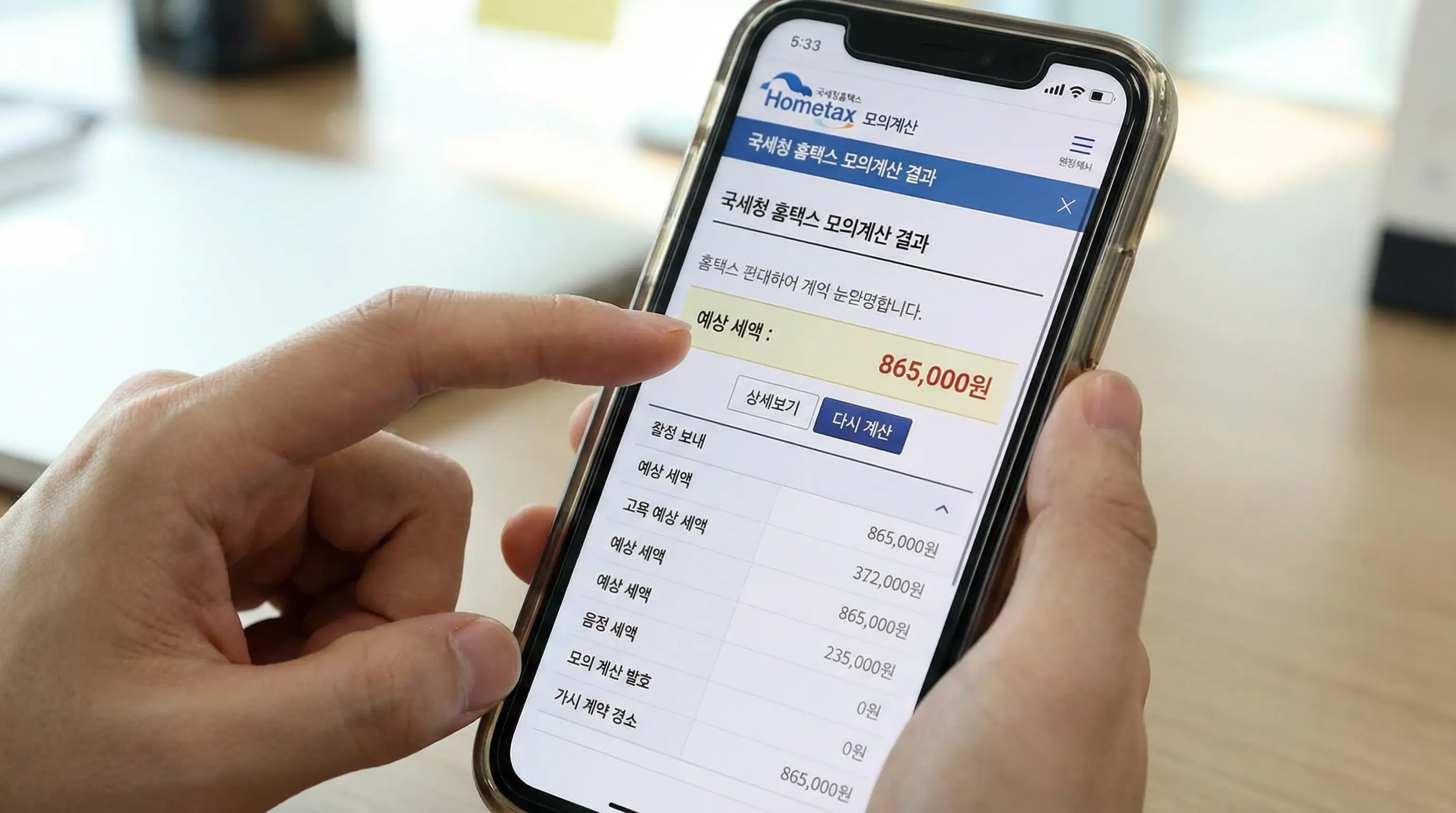 스마트폰 화면에 국세청 홈택스 모의계산 결과 화면이 뜨고 예상 세액을 확인하는 손가락 제스처