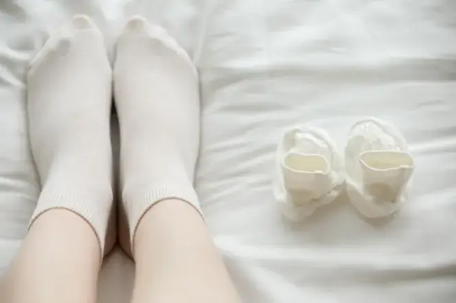 흰 침대 위에 누운 채 흰양말을 신은 사람의 발과 옆에 놓인 흰색 양말 한 켤레