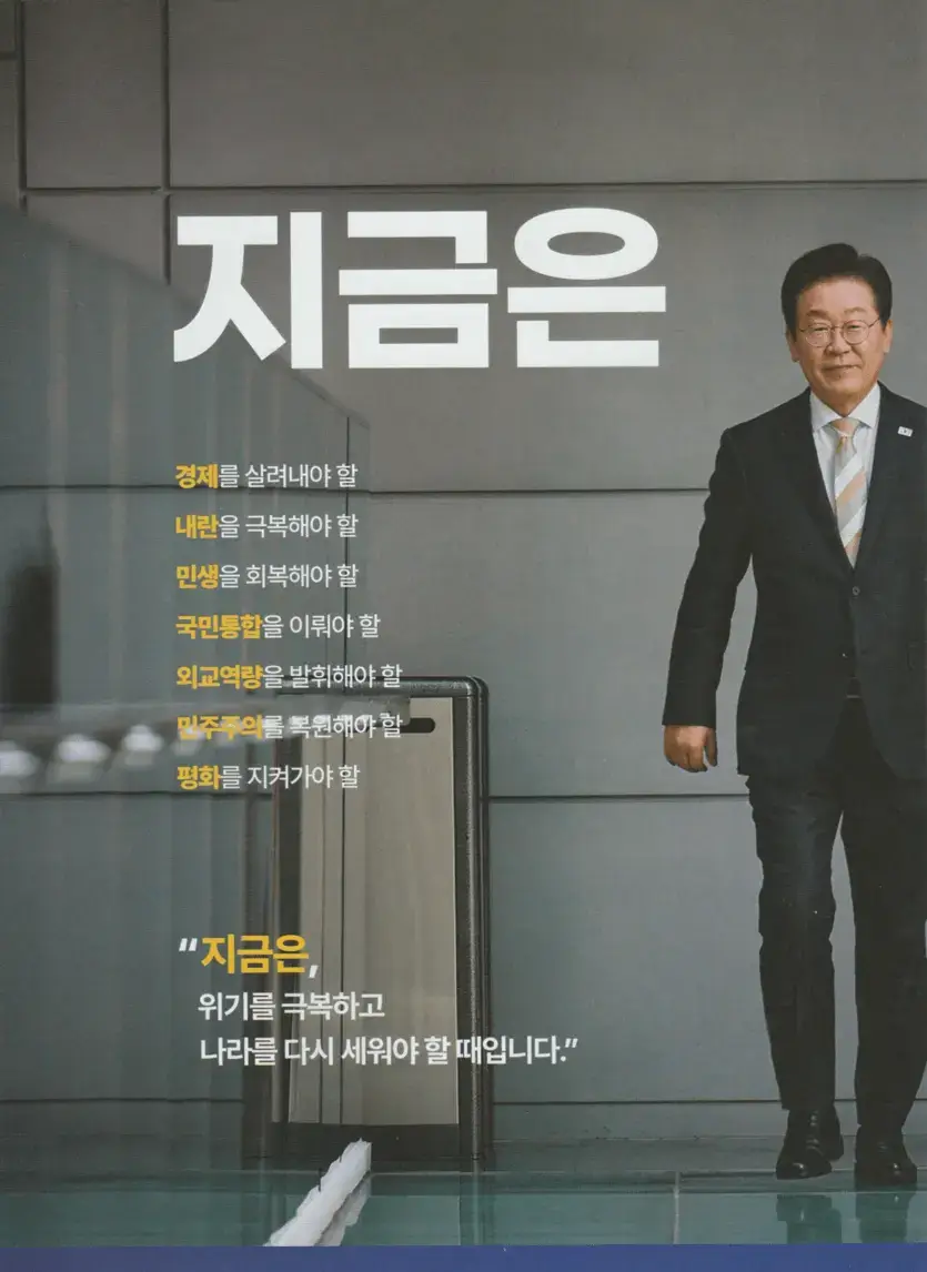 이재명 후보가 정장을 입고 밝은 표정으로 걸어오는 모습&amp;#44; 배경에는 &amp;#39;지금은&amp;#39;이라는 강조 문구와 함께 정책 방향성이 나열된 선거 포스터