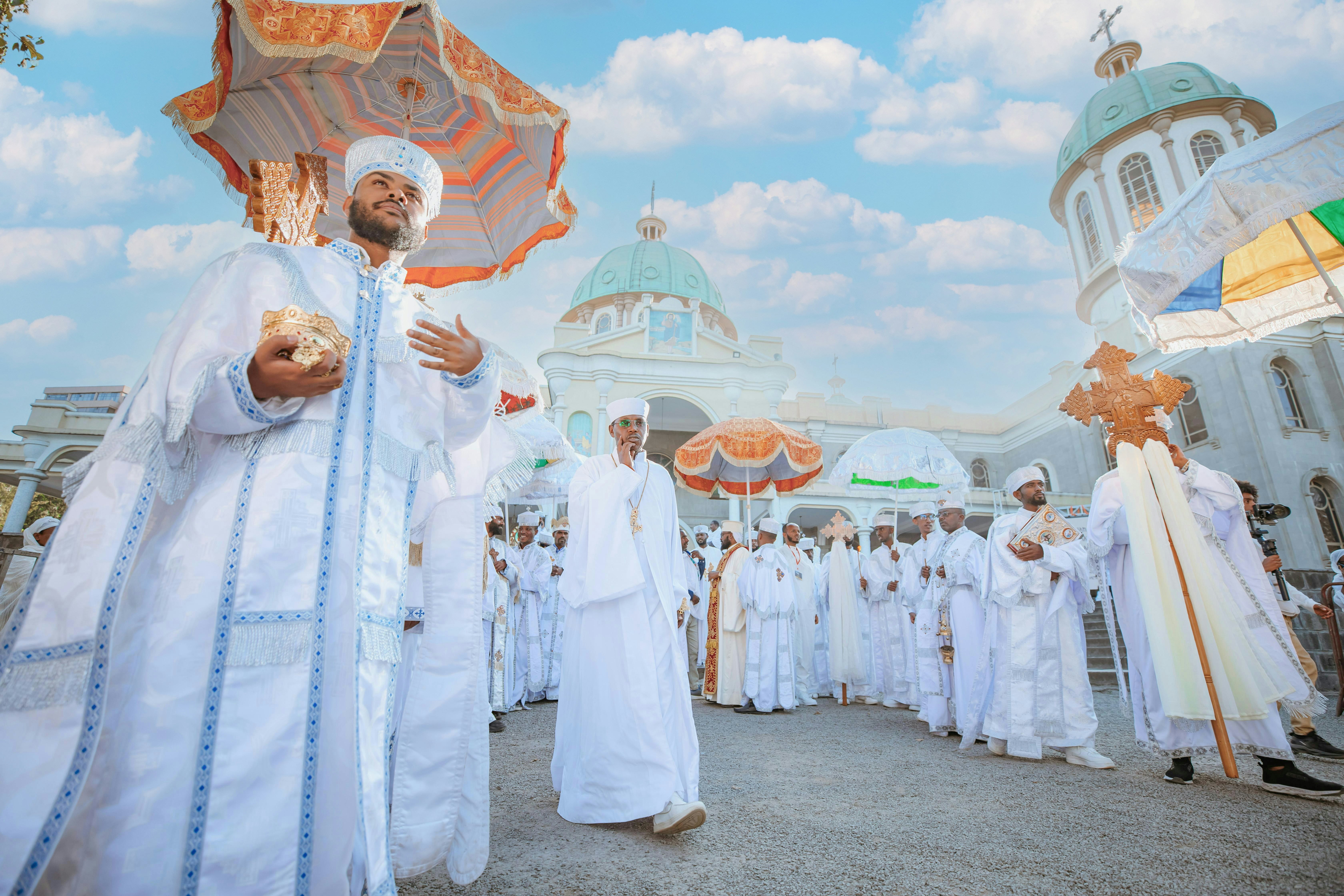 에티오피아 팀카트 축제에서 전통 의상을 입은 사람들이 화려한 우산과 십자가를 들고 성당 앞에서 행렬을 벌이는 모습