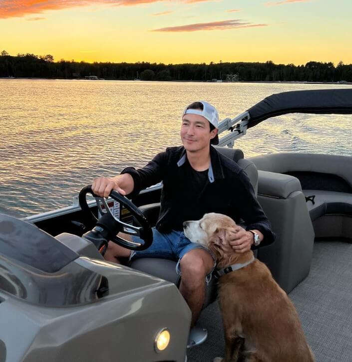 저녁-노을이-지고-있는-강에서-반려견과-함께-보트를-운전하는-다니엘-헤니의-사진