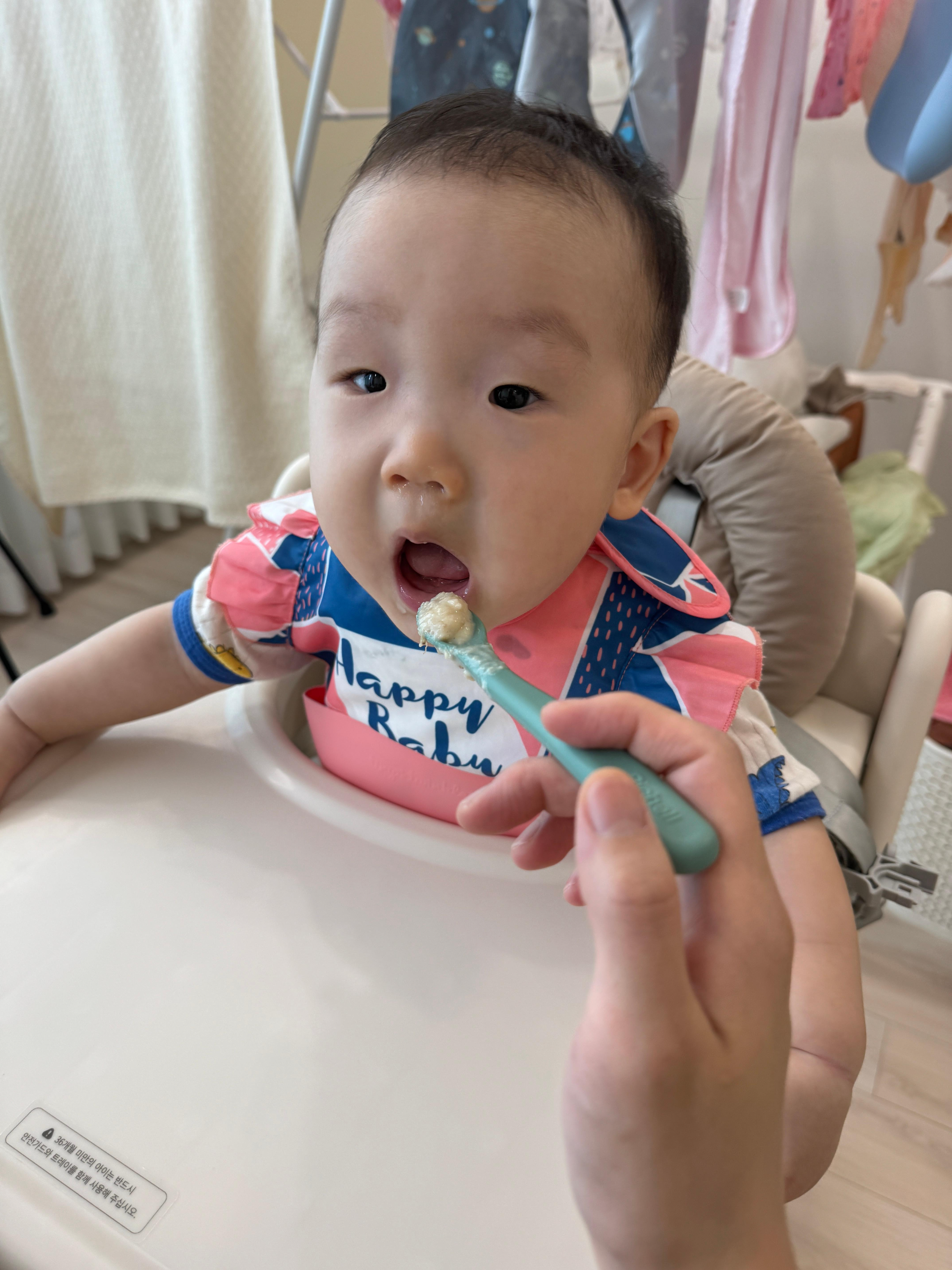 의자에 앉아 엄마가 수저로 오트밀+바나나+치즈를 떠서 먹여주니까 입을 벌리고 맞이하는 찬솔이의 클로즈업