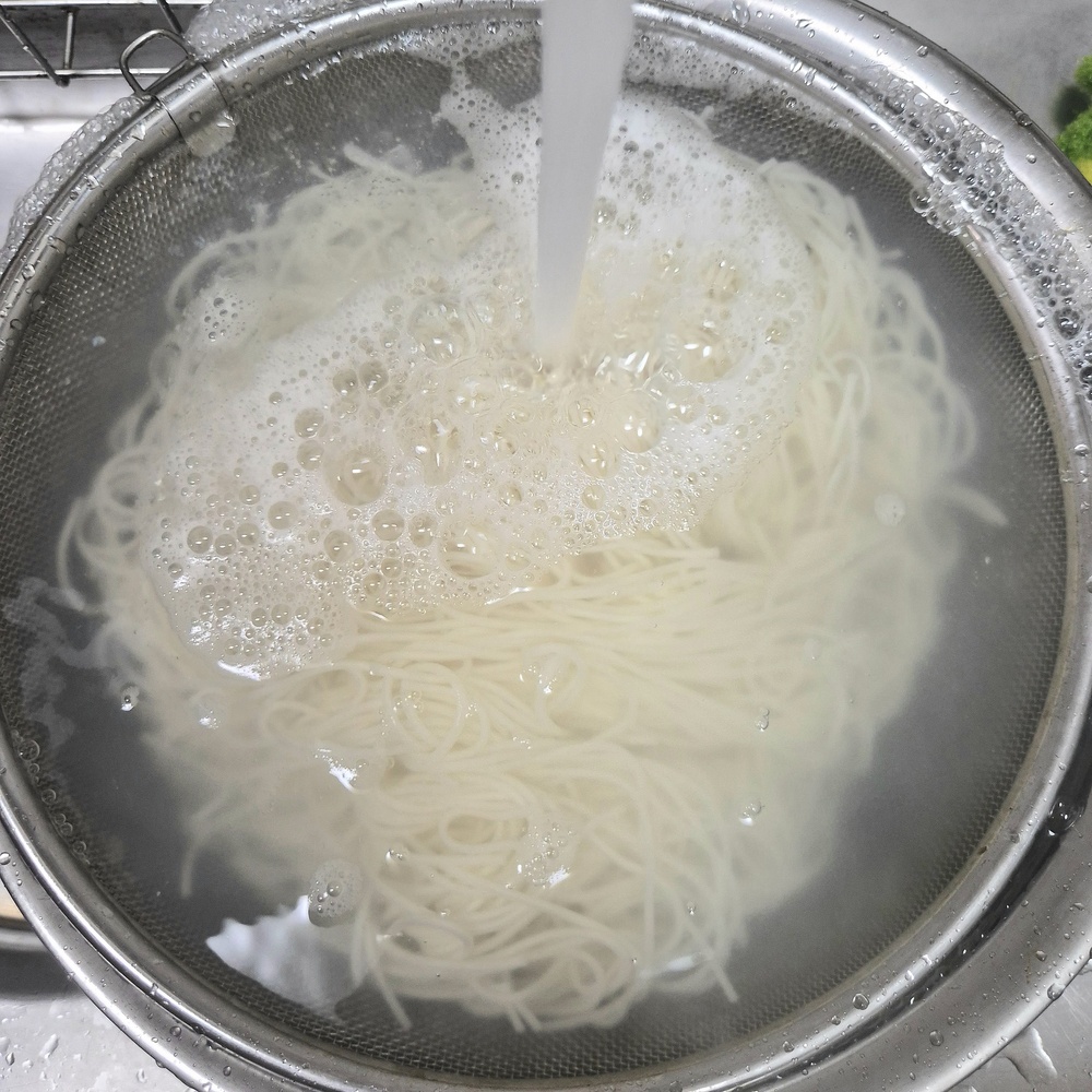 삶은 소면을 채반에 담아 찬물로 헹구는 모습