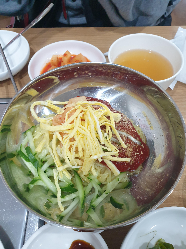 냉면 위에 계란과 오이 그리고 다진 얀념이 올려져 있다.