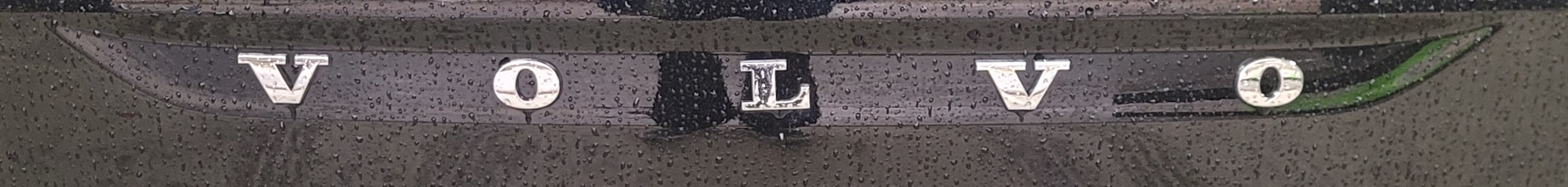 비를 맞은 차량 후면의 삐뚤어진 볼로 레터 엠블렘 모습이다.