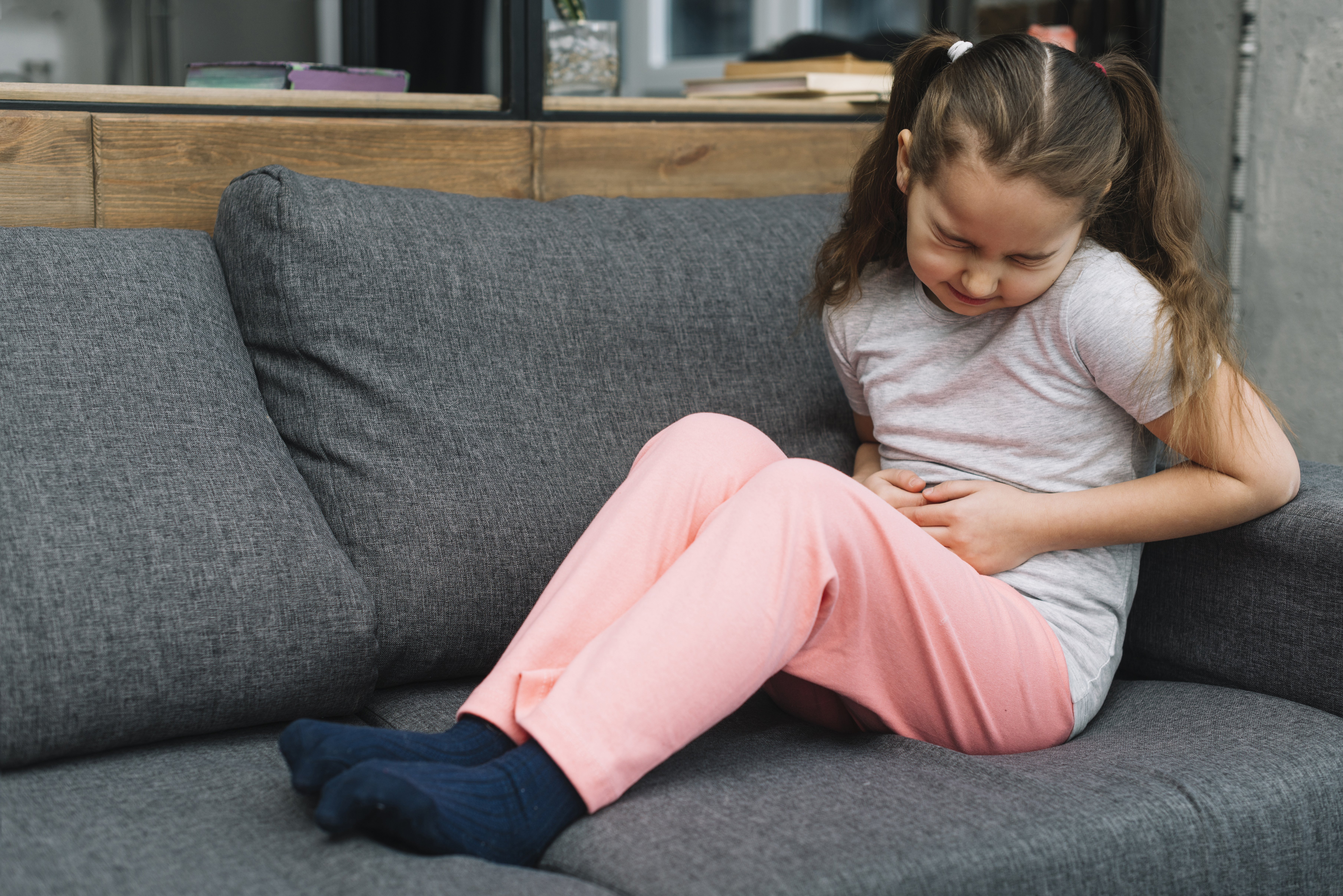 sick-girl-sitting-gray-sofa-suffers-from-stomach-pain-home