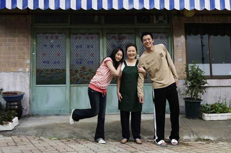 영화 해바라기에서 주인공 오태식이 어머니와 여동생과 함께 식당 앞에서 행복하게 웃고 있는 장면