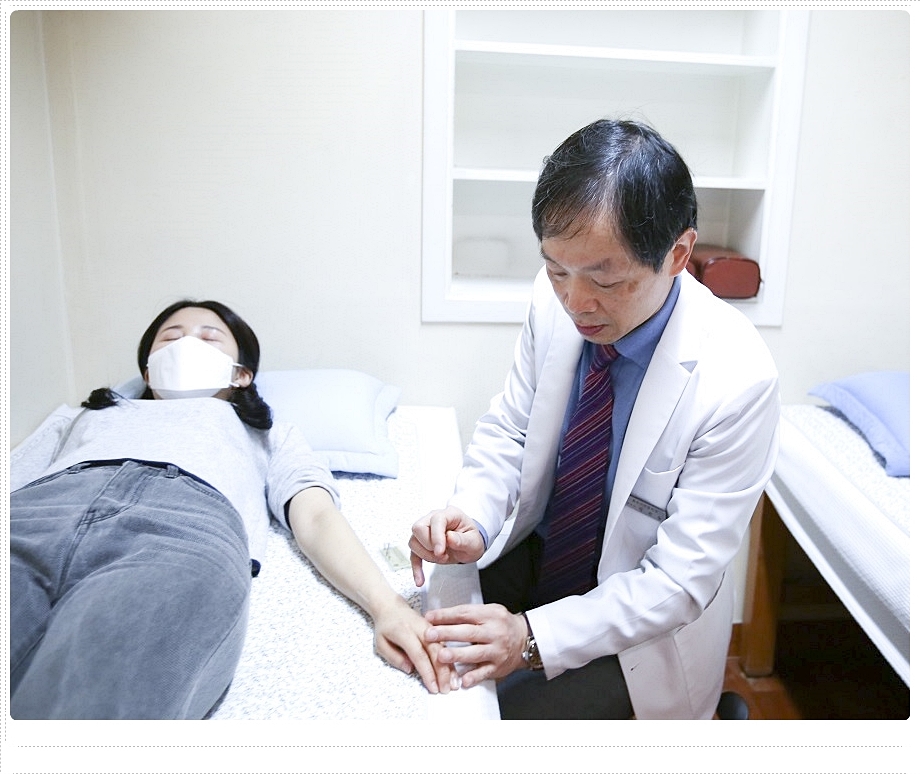 누워있는 환자의 손등에 침을 놓고 있는 한의사