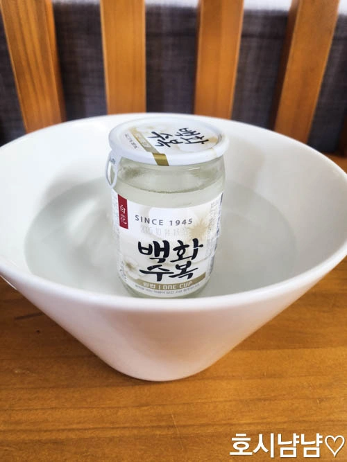 백화수복 원컵을 큰 흰색 그릇에 넣고 뜨거운 물로 중탕하는 모습. 따뜻하게 마시기 위한 백화수복 중탕 준비 과정.