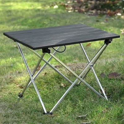 캠핑용 접이식 테이블 검은색이 풀밭위에 펼쳐져 있다.