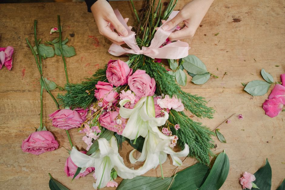 From above of crop anonymous woman tying bow on bouquet of fresh flowers placed on wooden table