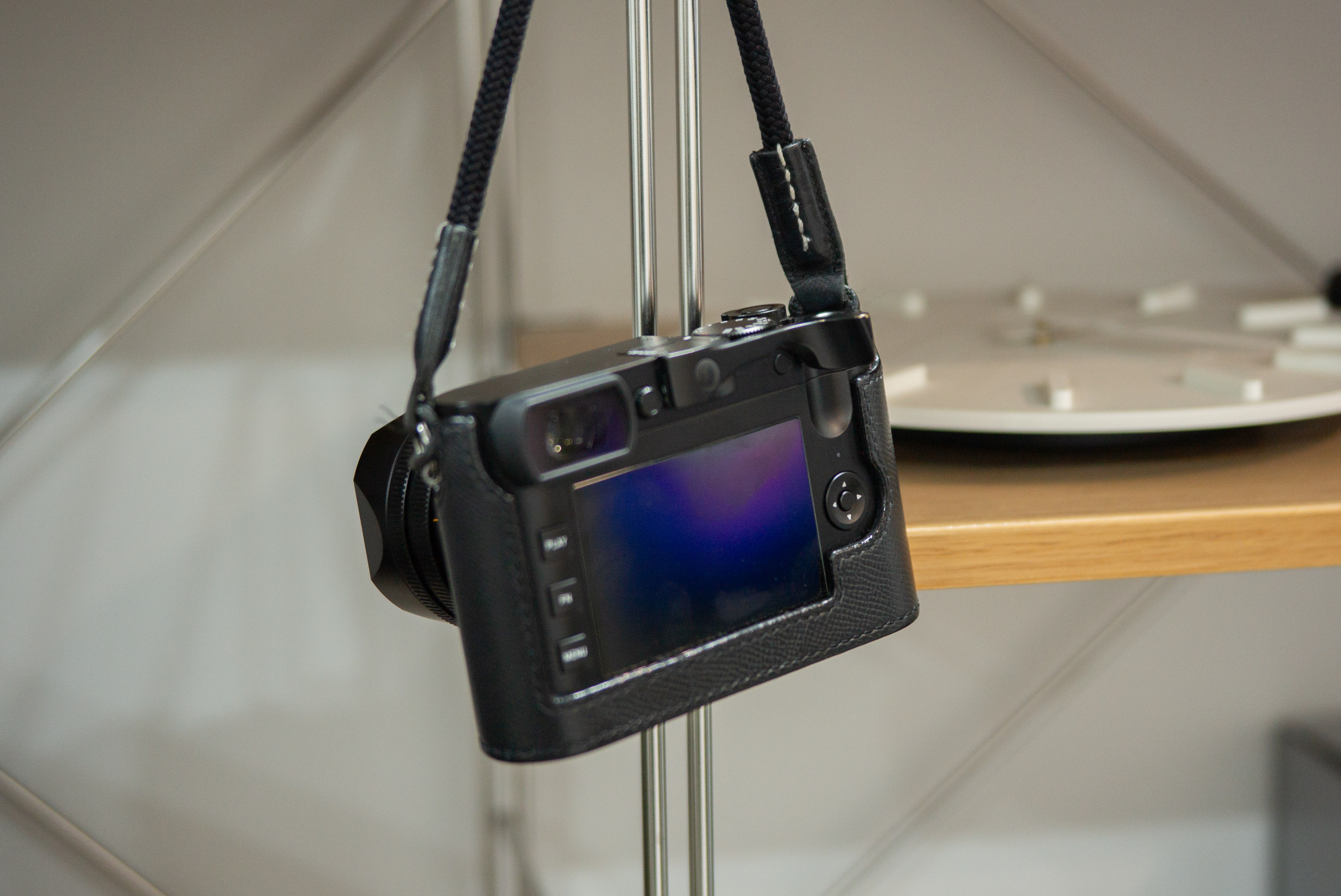 썸업 엄지그립이 핫슈에 결합된 라이카 Q2가 뒷면이 보이게 벽에 걸려있다.