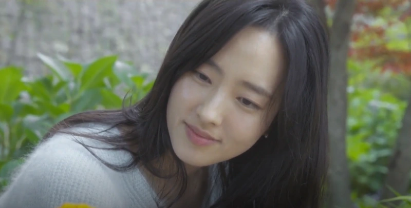 어느 정원을 배경으로 긴 검은 머리에 흰 티셔츠를 입고 앉아 있는 드라마 유괴의 날 소유진 캐릭터