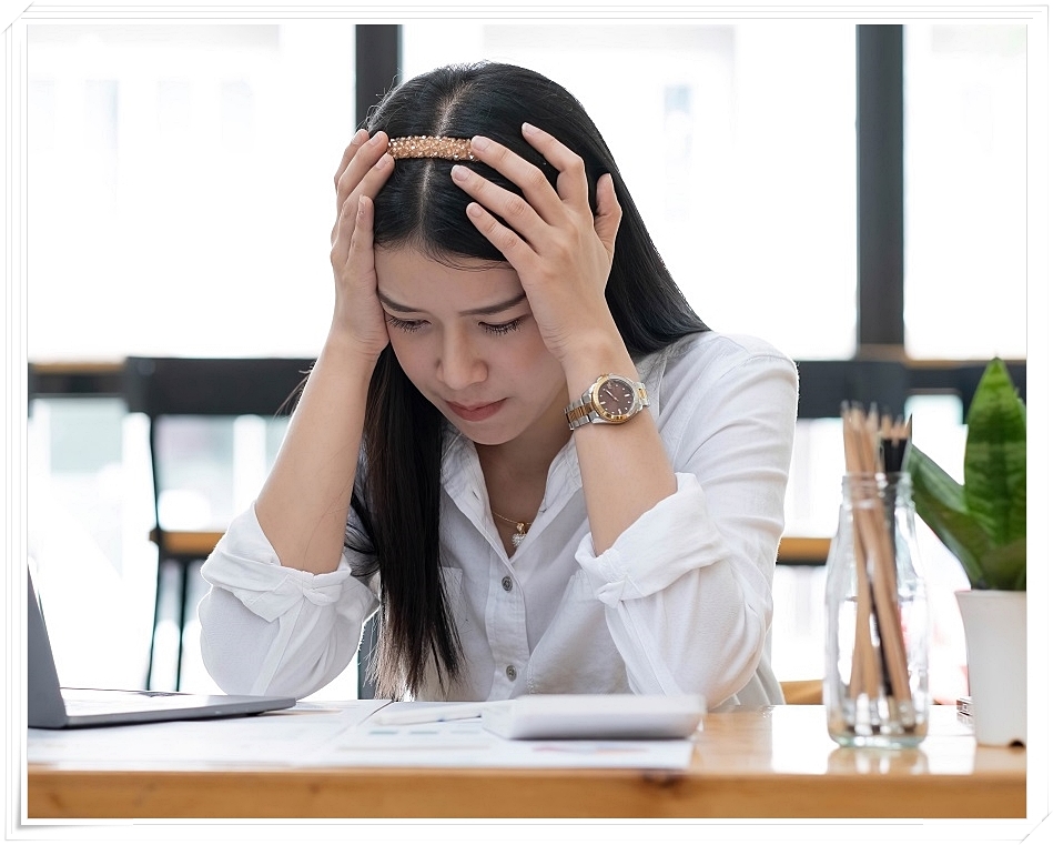 두 손으로 양 쪽 머리를 감싼 채 다소 힘겨운 표정을 짓고 있는 여성의 모습