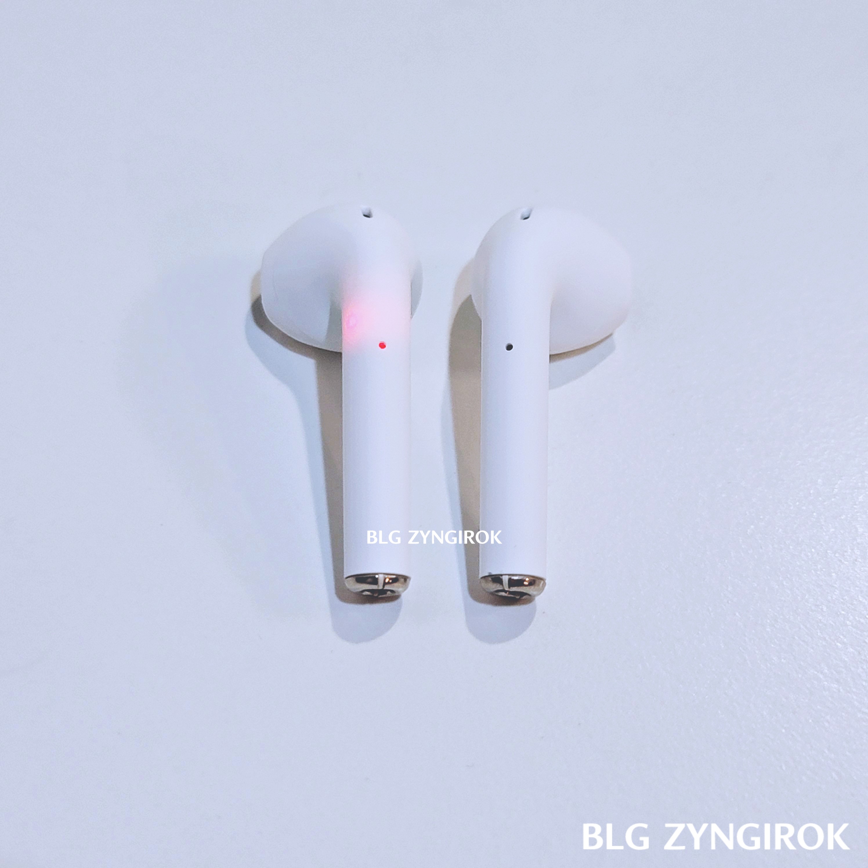 다이소 무선 블루투스 이어버즈 2개가 테이블 위에 놓여있는 모습이다. 왼쪽 이어버즈는 몸통에 빨간 LED 불이 들어온 모습이다.