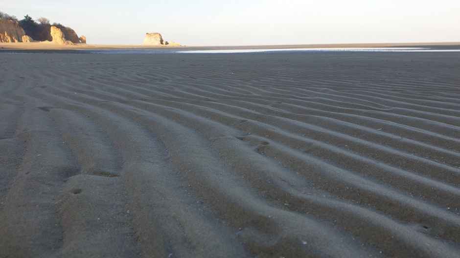 대청도 해안의 넓은 모래사장. 고운 모래결이 바람에 만들어낸 물결 무늬가 선명하며, 먼 바다와 기암절벽이 어우러진 서해 특유의 한적한 해변 풍경.