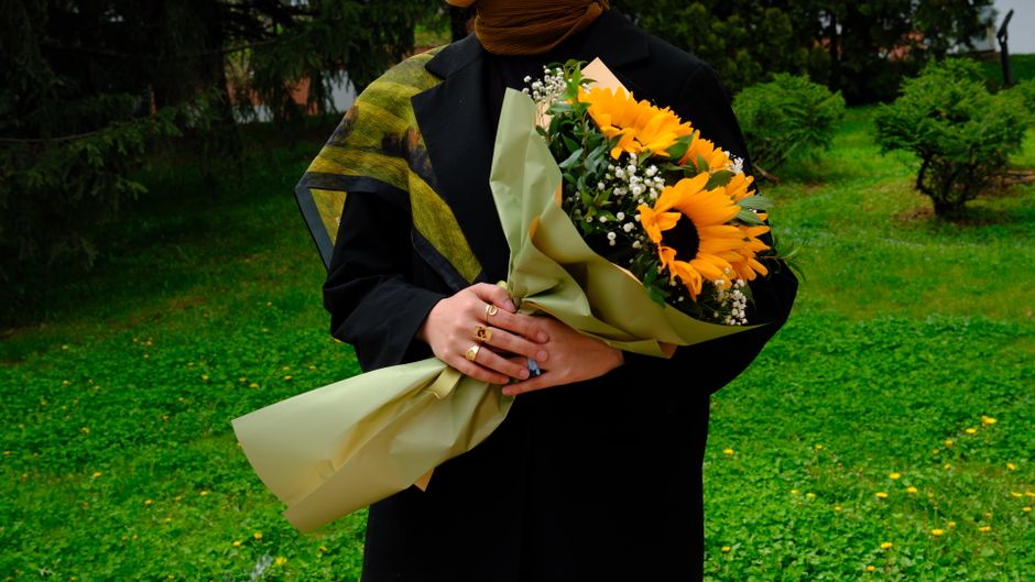 A person in dark clothing holding a vibrant sunflower bouquet in a green park.