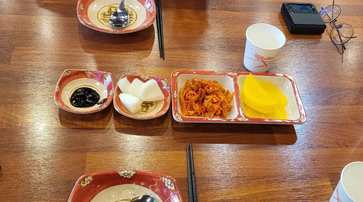 보배반점 -
나무테이블 위 양쪽 앞접시와 숟가락, 젓가락이 놓이고 가운데 접시에 담긴 검은색 춘장과 흰색 양파, 주황색짜사이, 노란 단무지
