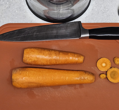 당근 두 개가 도마 위에 놓여 있고, 칼과 함께 썰 준비를 하고 있다.