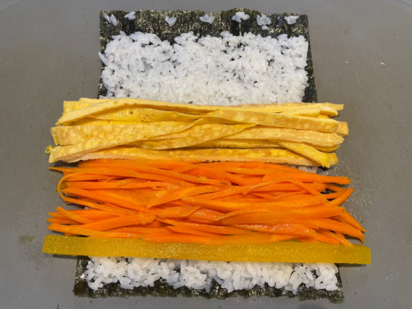 Placing pickled radish, egg, and carrot on rice