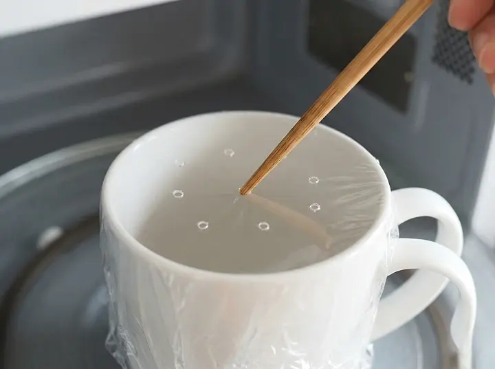 머그컵 술빵 반죽 위에 랩을 씌우고 젓가락으로 구멍 6개를 뚫는 모습 &mdash; 전자레인지 가열 시 증기를 배출하는 핵심 단계