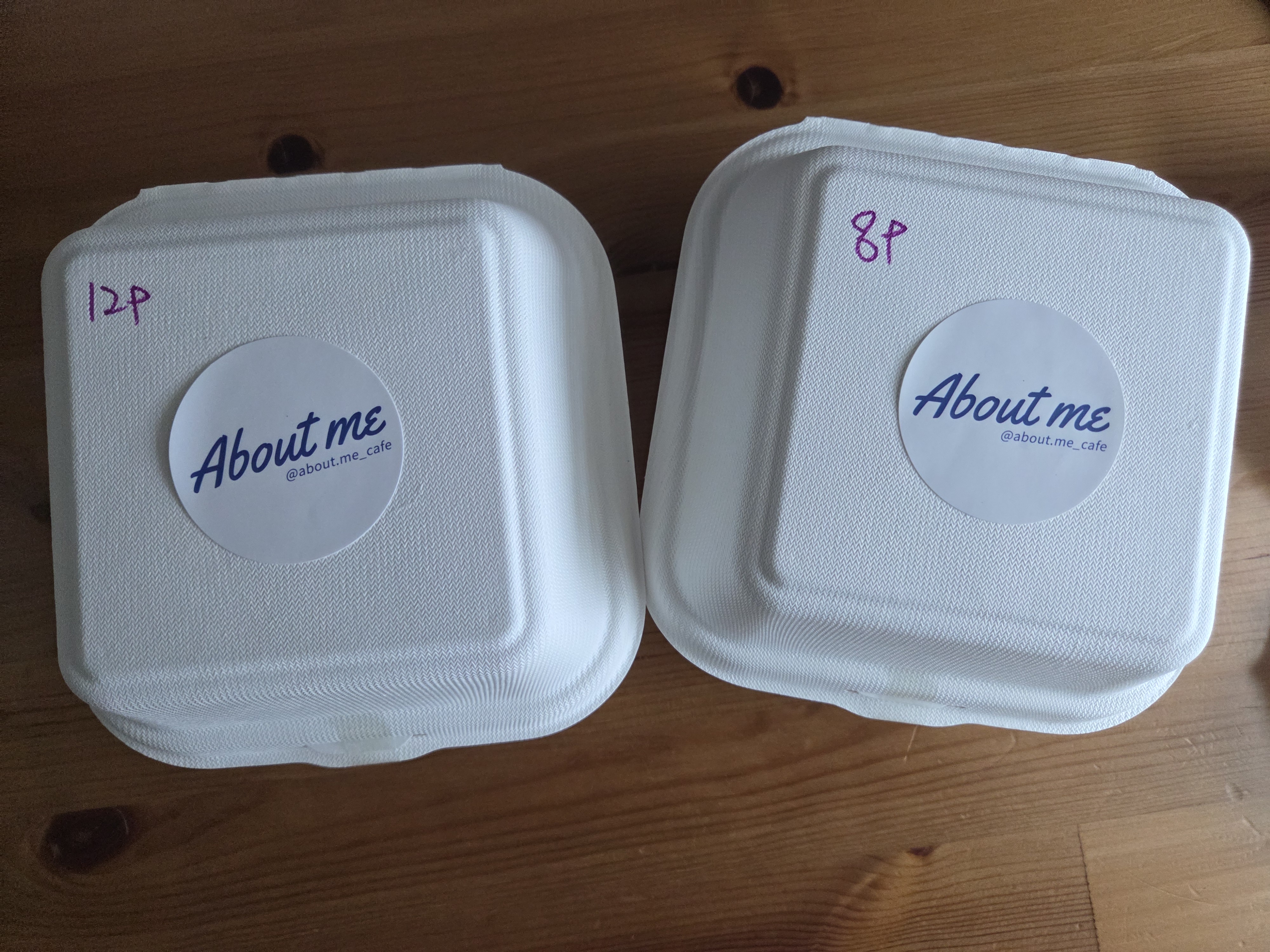 까치산역 카페 어바웃미 배달 포장 박스 두 개, 하얀 친환경 용기 위에 About me 로고 스티커가 붙어 있는 모습