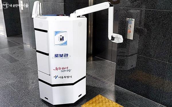 로보관이 스스로 팔을 뻗어 엘리베이터 버튼을 누르고 있다.