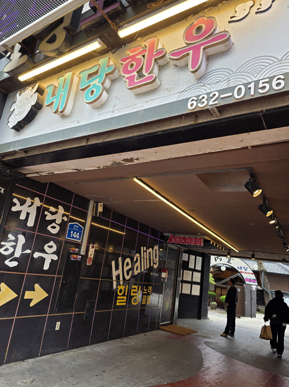 내당 한우 간판과 힐링 노래클럽 안내 벽면이 보이는 골목 입구
