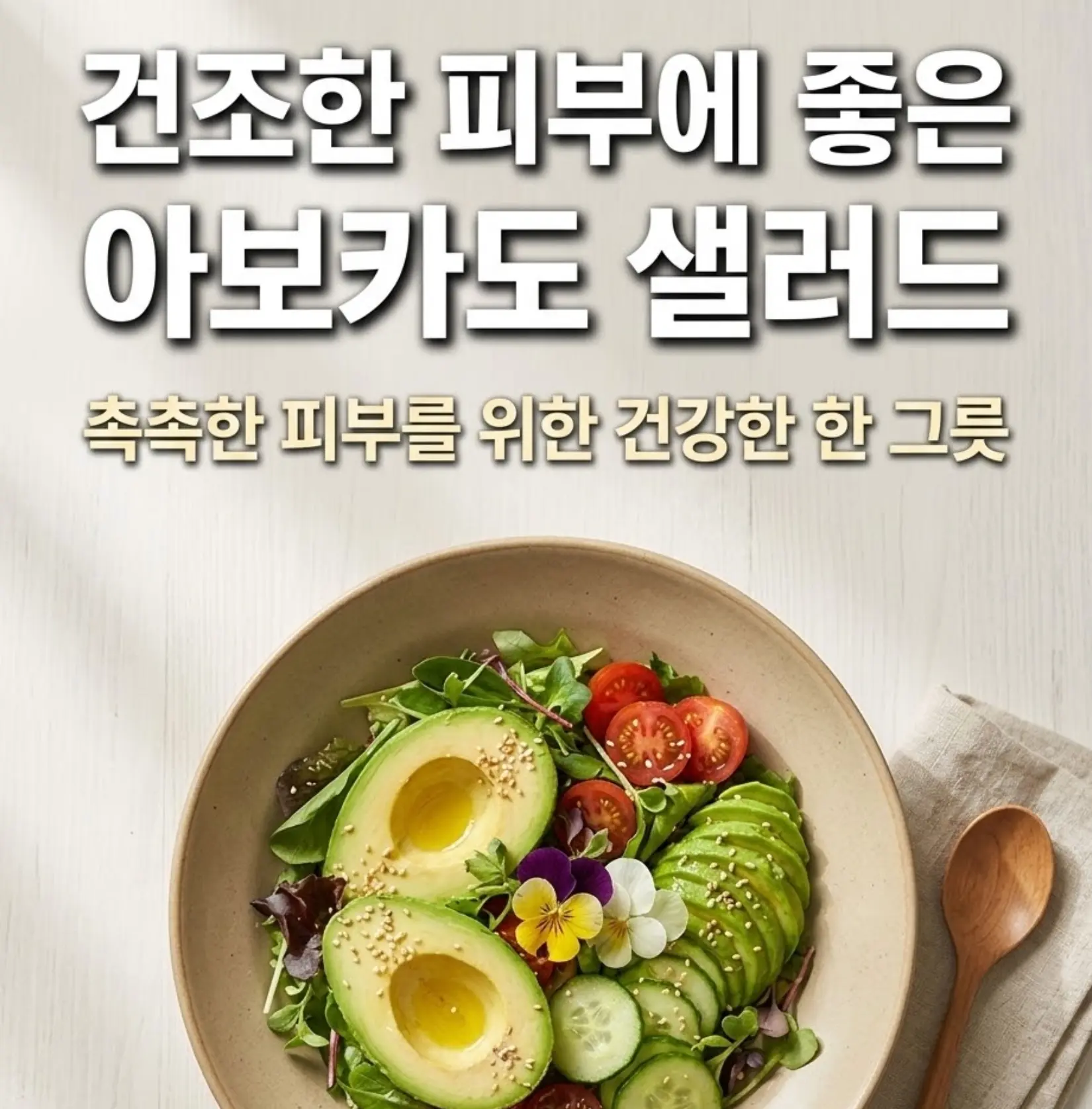 넓고 낮은 아이보리 도자기 그릇에 담긴 아보카도 샐러드. 반으로 자른 아보카도, 방울토마토, 오이 슬라이스 위에 참깨와 식용 꽃으로 장식하고 올리브오일을 뿌린 모습. 나무 숟가락과 린넨 냅킨이 옆에 놓여 있음.