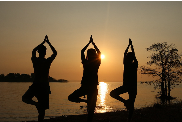 석양을 배경으로 세 사람이 요가 나무 자세를 하며 균형을 잡고 있는 모습. 건강한 생활습관과 심리적 안정을 상징한다.