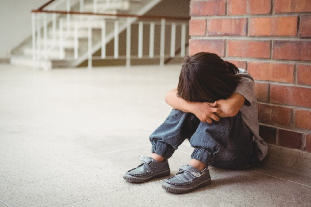 한 남자아이가 몸을 웅크린 채 머리를 숙이고 있다.