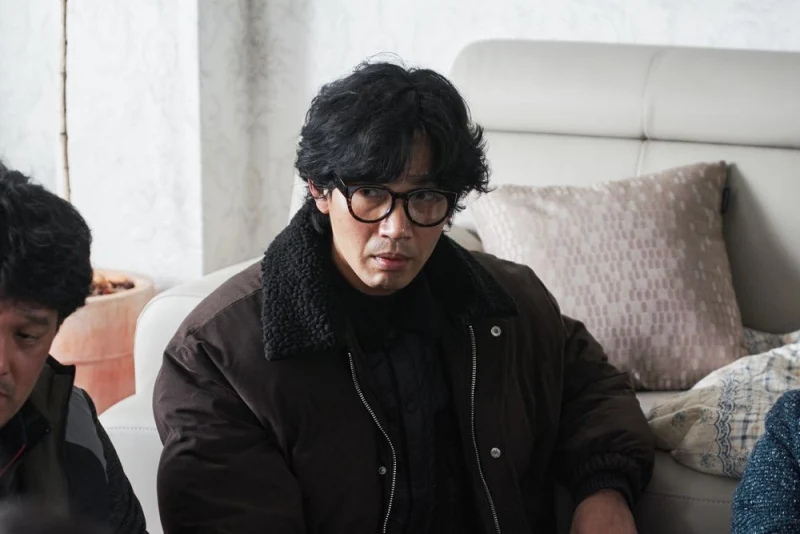 어느 아파트 실내에 허름한 옷과 뿔테 안경을 쓴 도균