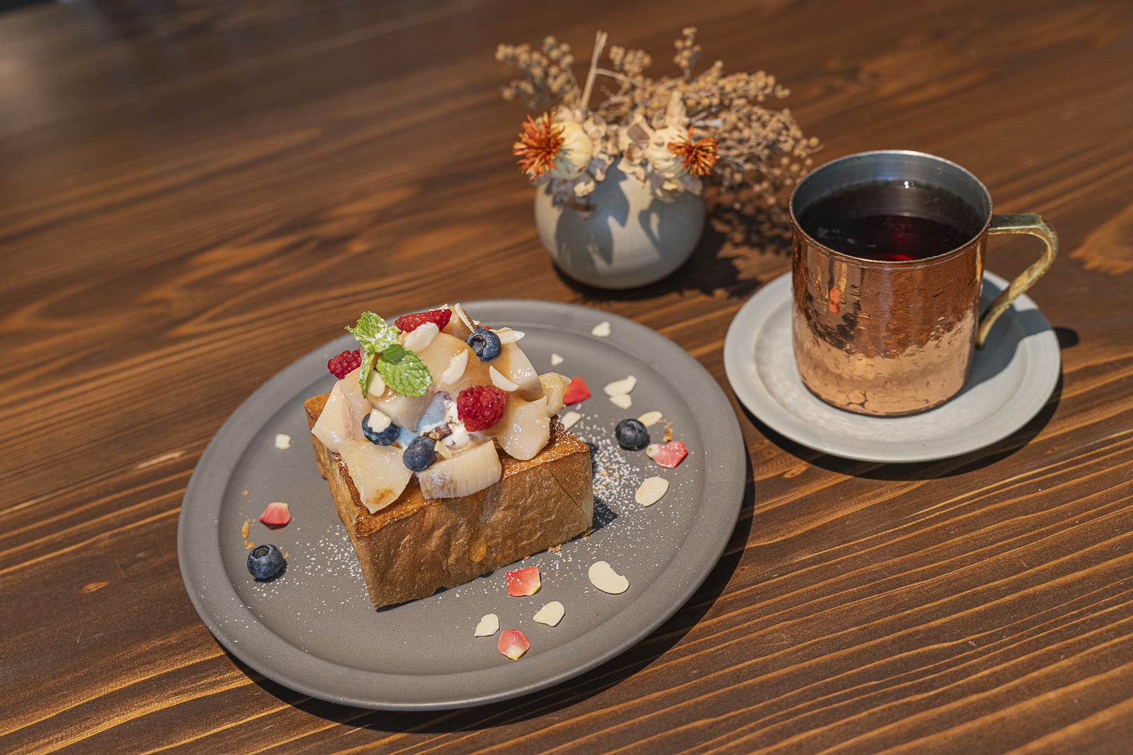 LIGNUM: thick toast piled with fruit and cream, and a drink in a copper-colored mug on a wooden table.
