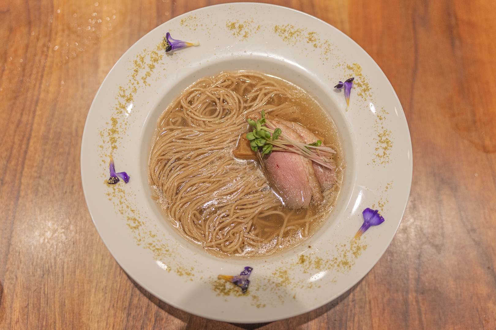 Gion Duck Noodles: noodles in clear brown broth with meat and vegetables, and purple flowers around a broad white rim.