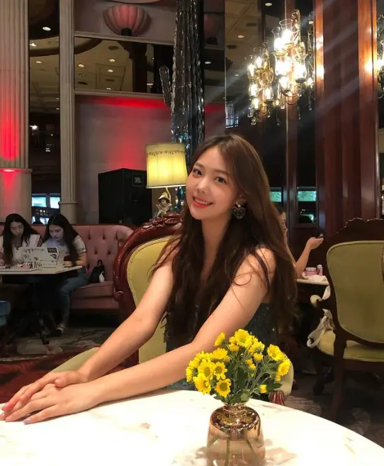 솔로지옥 3- 흰테이블 두팔을 앞으로 쭉 뻗고 검은 민소매 원피스를 입고 의자에 안자 카메라를 보고 미소짓는 여자출연자 조민지