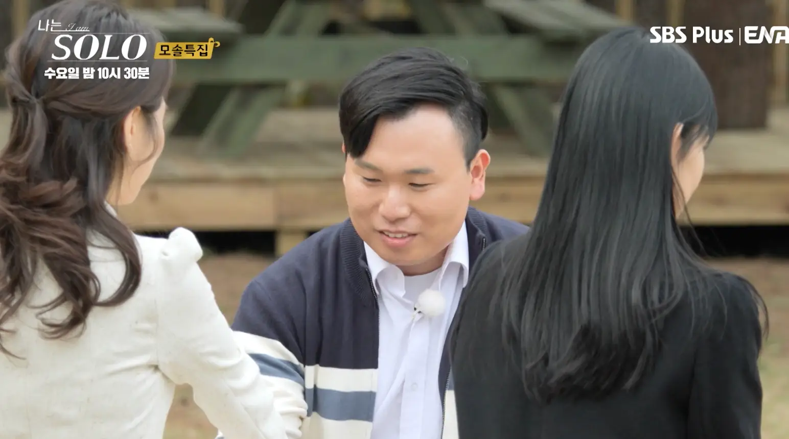 솔로- 파란 가디건을 입고 흰셔츠를 입은채 흰옷을 입은 여자에게 손을 건네며 미소짓는 영호