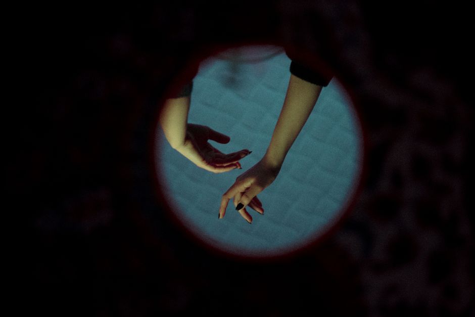 A creative close-up photograph of hands reaching, viewed through a circular frame in low light.