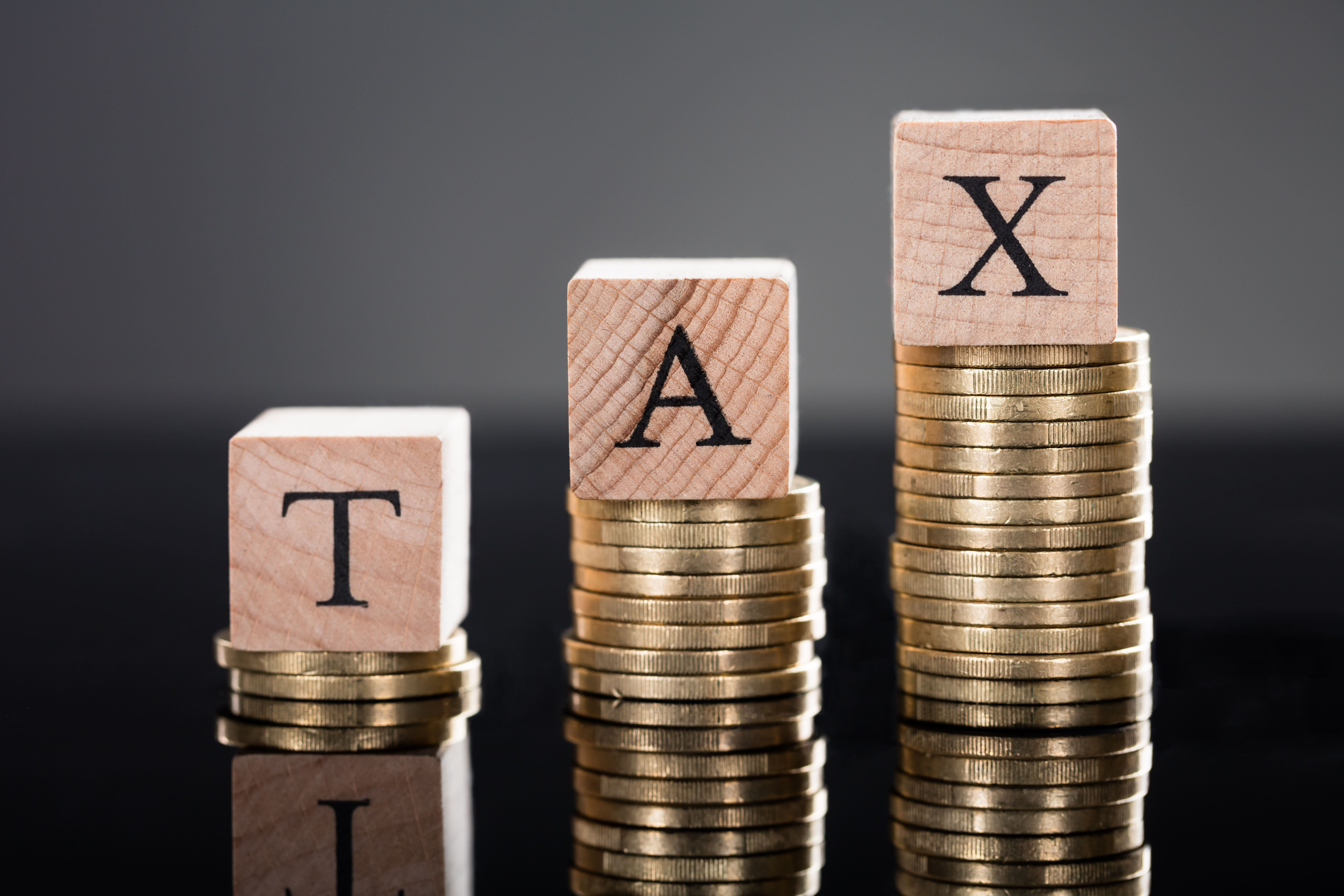 동전 위에 쌓인 TAX 글자 블록으로 세금을 상징하며, 부가가치세, 종합소득세, 원천세 등 다양한 세금 종류를 표현한 이미지, 세금 관리와 절세의 중요성 강조