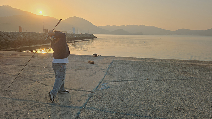 노을지는 바닷가에서 낚시대를 던지는 남자아이