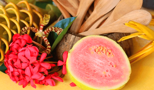 반으로 자른 분홍색 과육을 보이는 구아바와 옆에는 빨간 꽃이 있고, 위에는 나무 주걱들이 가득하다.