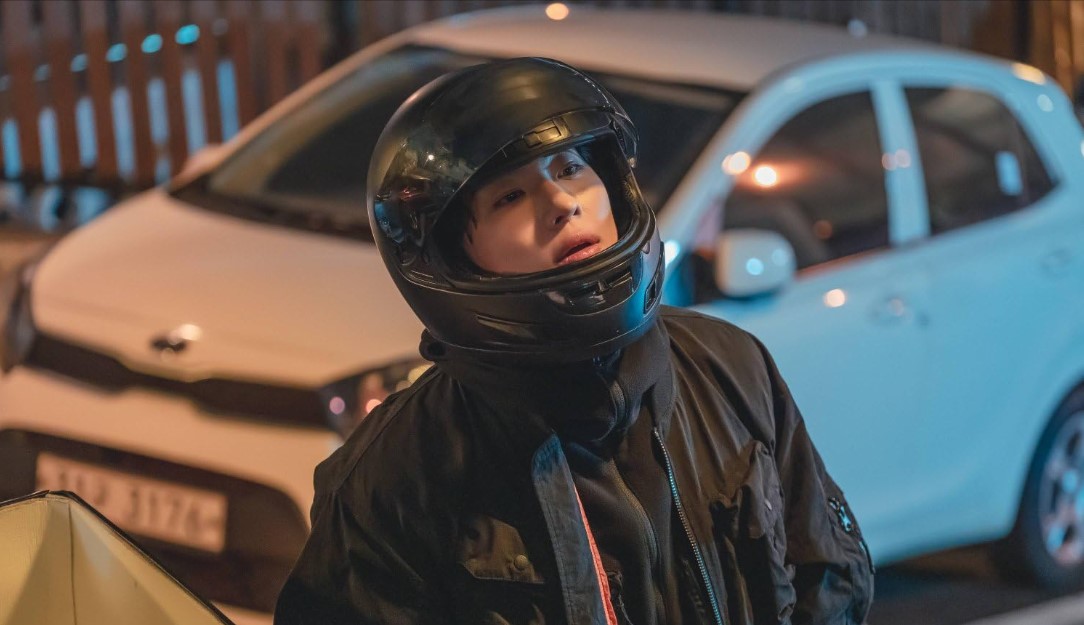 넷플릭스 영화 타로 스틸컷｜헬멧을 쓴 남성이 배달 가방 앞에서 멍하니 서 있는 장면｜불길한 사건의 시작을 암시하는 긴장감 있는 순간
