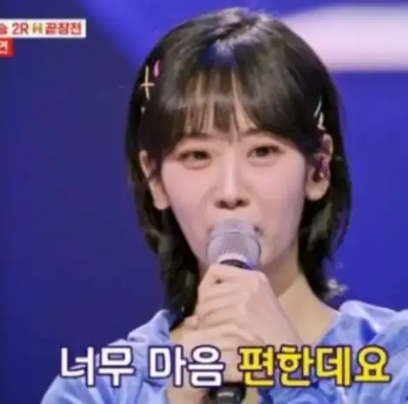 파란 무대배경 하늘색 옷을 입고 두손으로 마이크를 쥔채 노래하는 가수