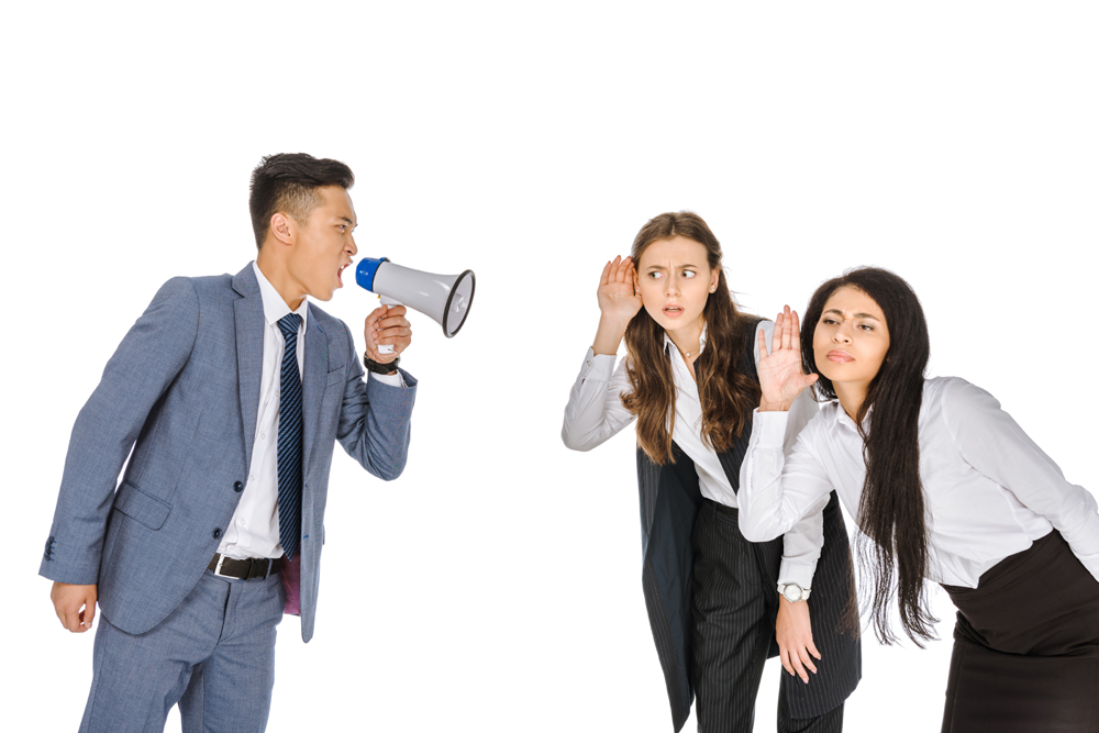 한 남성이 푸른색 정장을 입고 확성기를 들고 소리치고 있습니다. 그는 단호한 표정으로 메시지를 전달하려는 듯 보입니다. 반면, 두 여성은 흰색 셔츠를 입고 있으며, 그의 말을 잘 듣지 못하는 듯한 행동을 보입니다. 한 여성은 귀를 기울이며 혼란스러운 표정을 짓고 있고, 다른 여성은 몸을 앞으로 숙여 더 가까이 들으려는 자세를 취하고 있습니다.