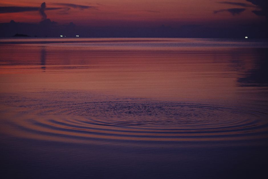 Captivating sunset over a calm lake with soft ripples and pink hues in the sky.