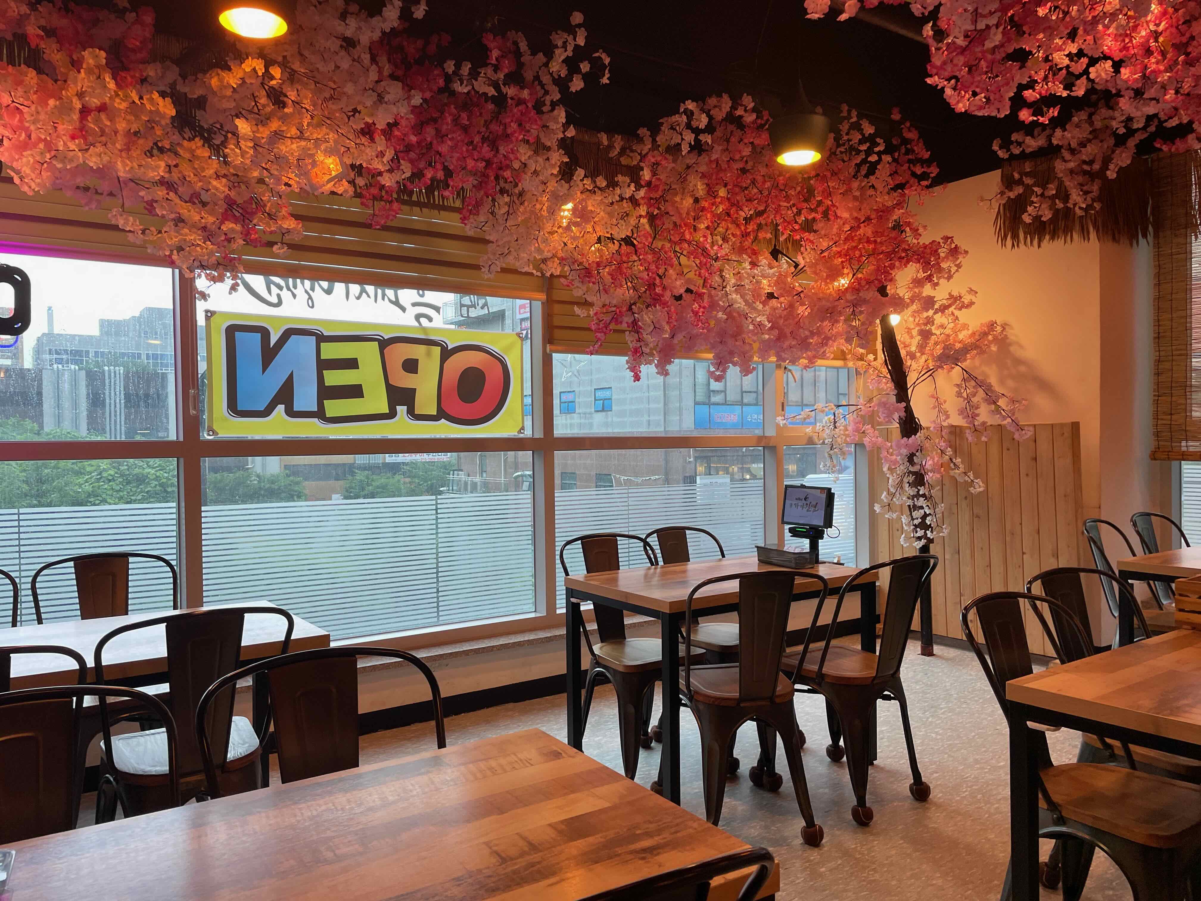 식당 내부모습 천장에 벚꽃 인테리어와 갈색 나무 테이블이 놓여있는 모습