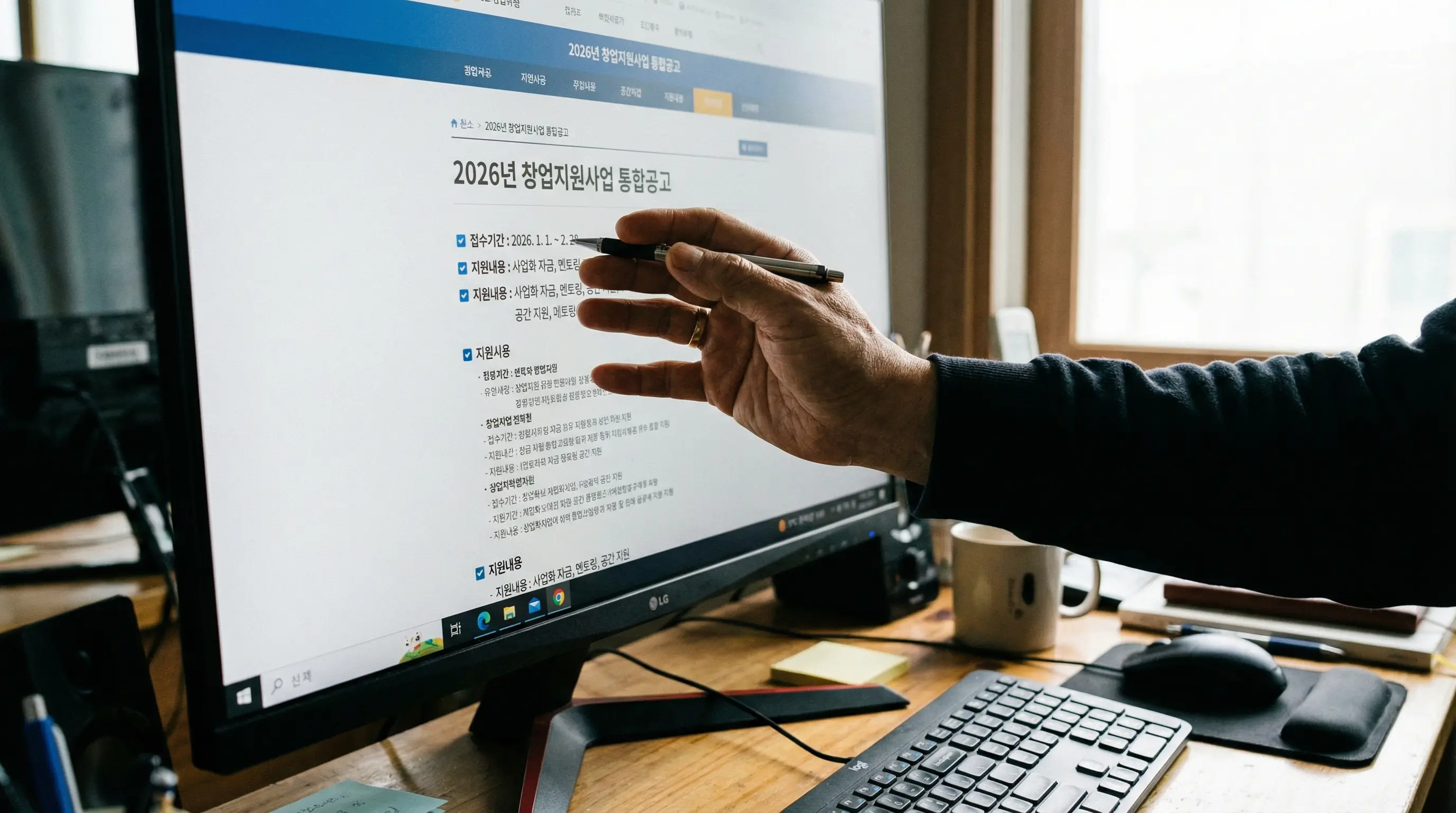 홈페이지를 모니터 화면에 띄워놓고 2026년 창업 지원 공고를 꼼꼼히 체크하는 창업가의 손 클로즈업