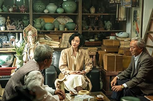 도자기와 골동품으로 가득한 방에서 중년 여성과 두 명의 노인이 앉아 진지하게 대화를 나누고 있는 장면