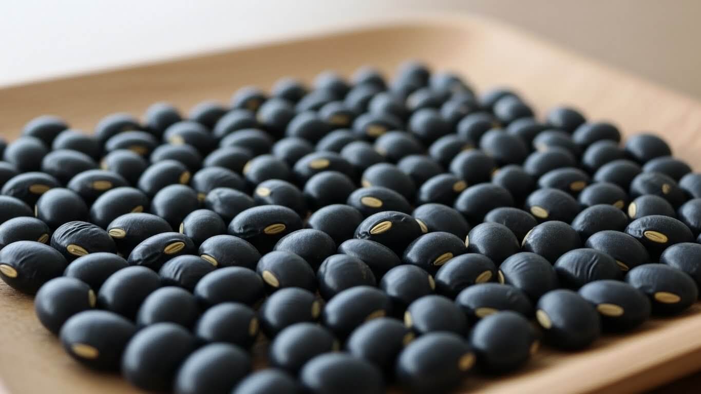 윤기 나는 검은 껍질과 황금빛 배꼽이 선명하게 보이는 서리태 원물이 나무 쟁반에 가지런히 담겨 있는 모습.